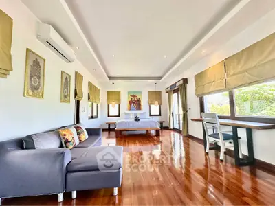 Spacious bedroom with elegant decor and polished wooden floors, featuring a cozy seating area and large windows.