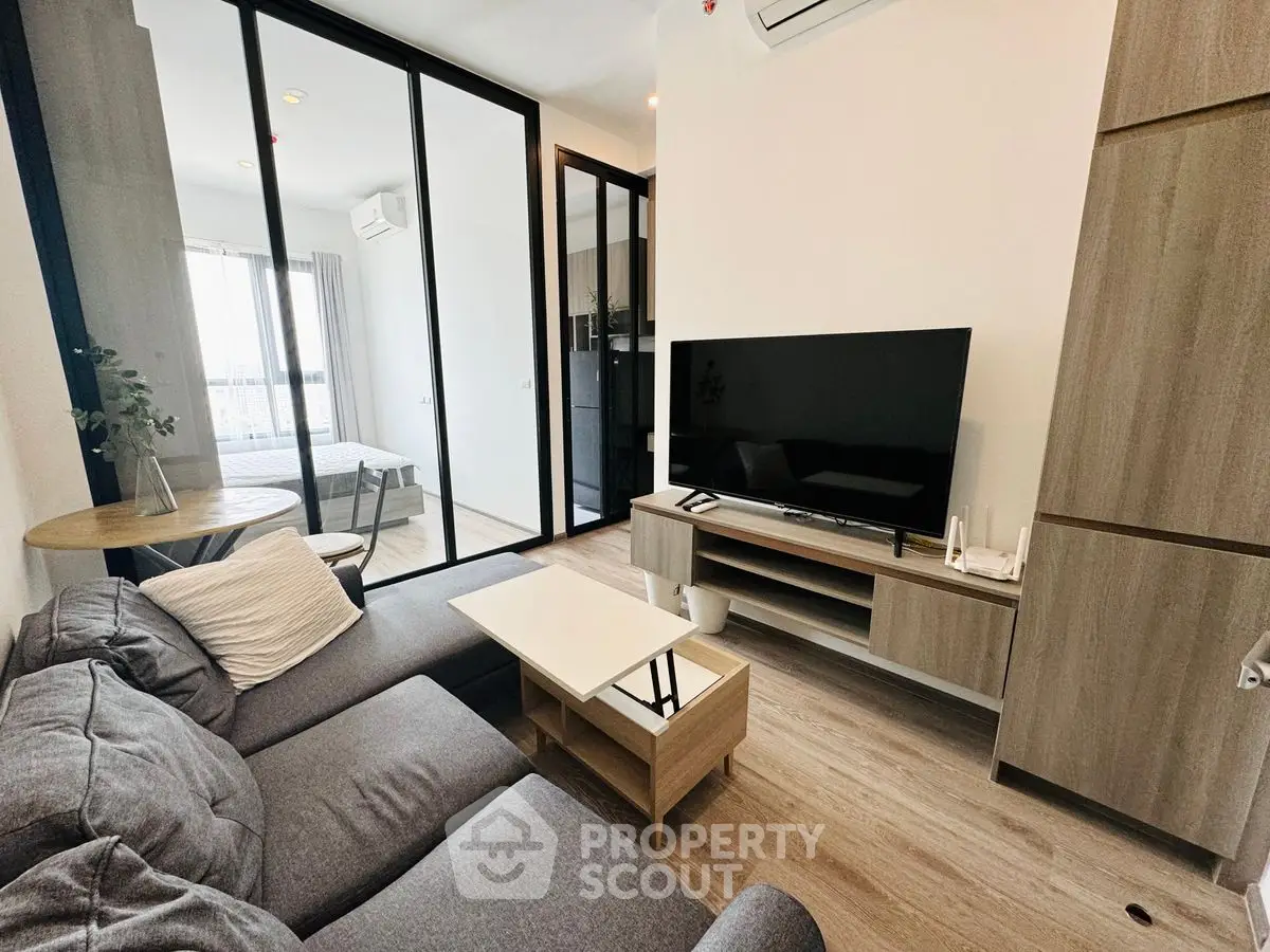 Modern living room with sleek furniture and large TV, open layout to bedroom.
