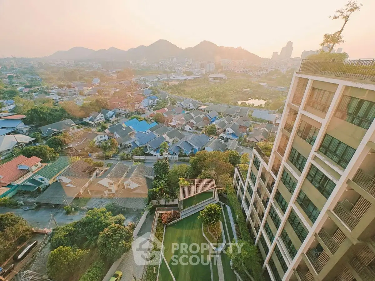 Stunning aerial view of urban landscape with modern building and scenic mountains at sunset.
