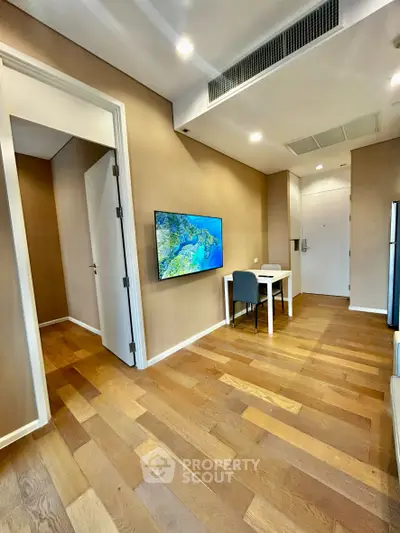 Modern apartment interior with wooden flooring, wall-mounted TV, and dining area.