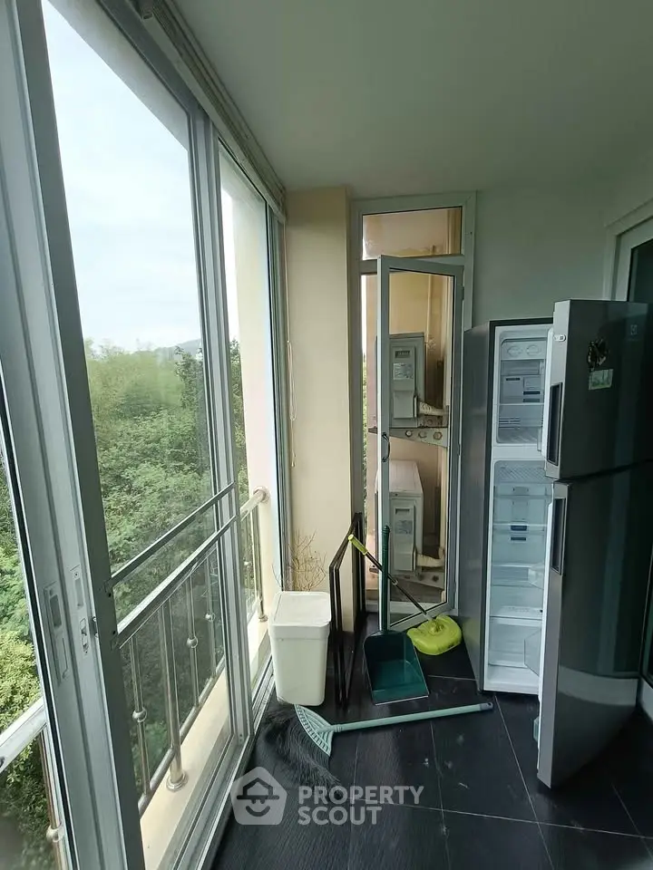 Bright balcony with sliding glass doors and a modern refrigerator, overlooking lush greenery.