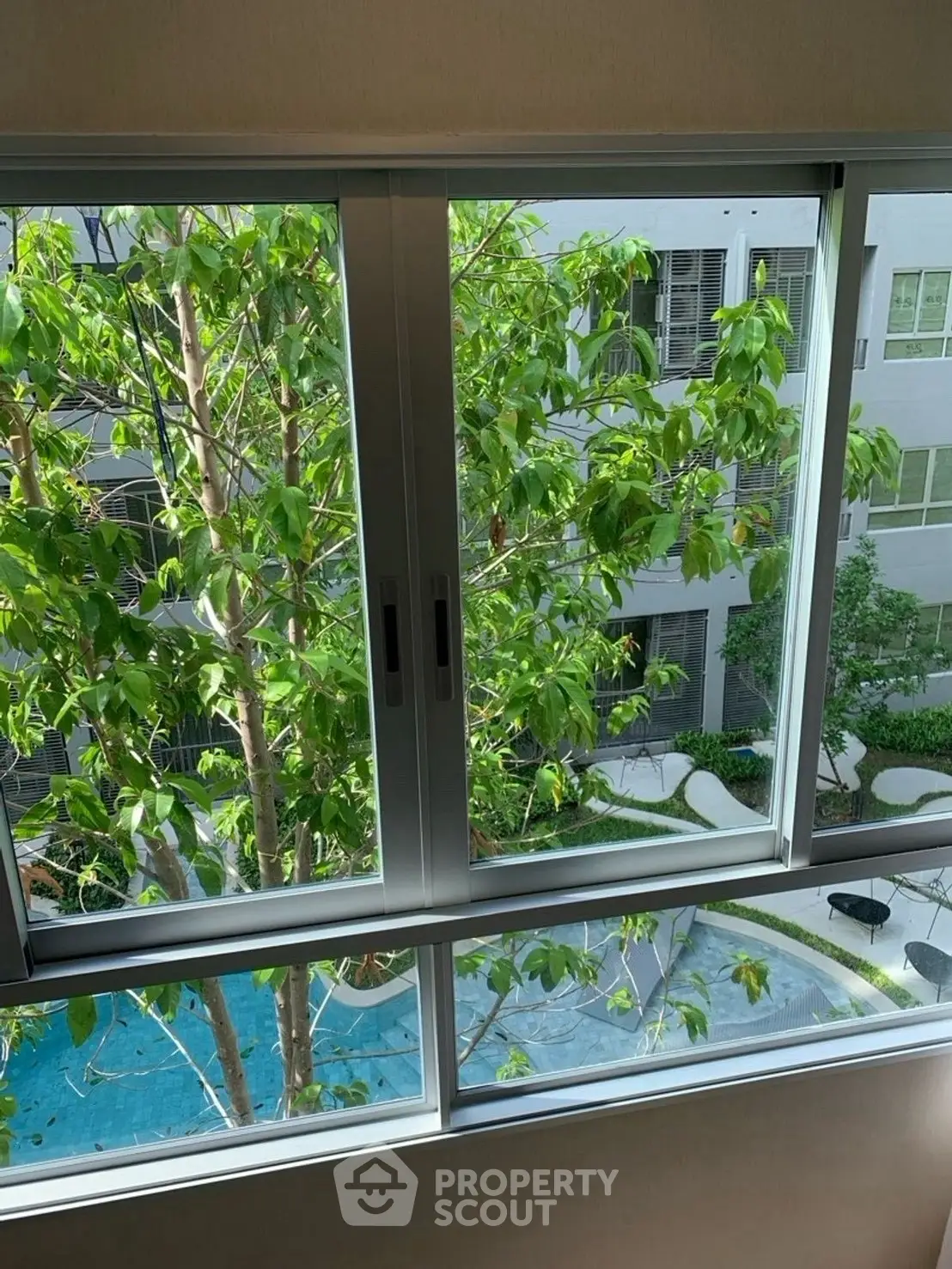 Modern apartment window view overlooking lush garden and pool area, offering serene and refreshing ambiance.