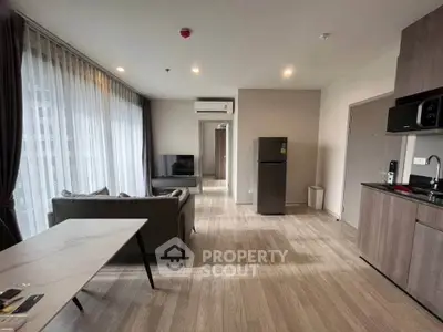 Modern living room with open kitchen, featuring sleek appliances and large windows for natural light.