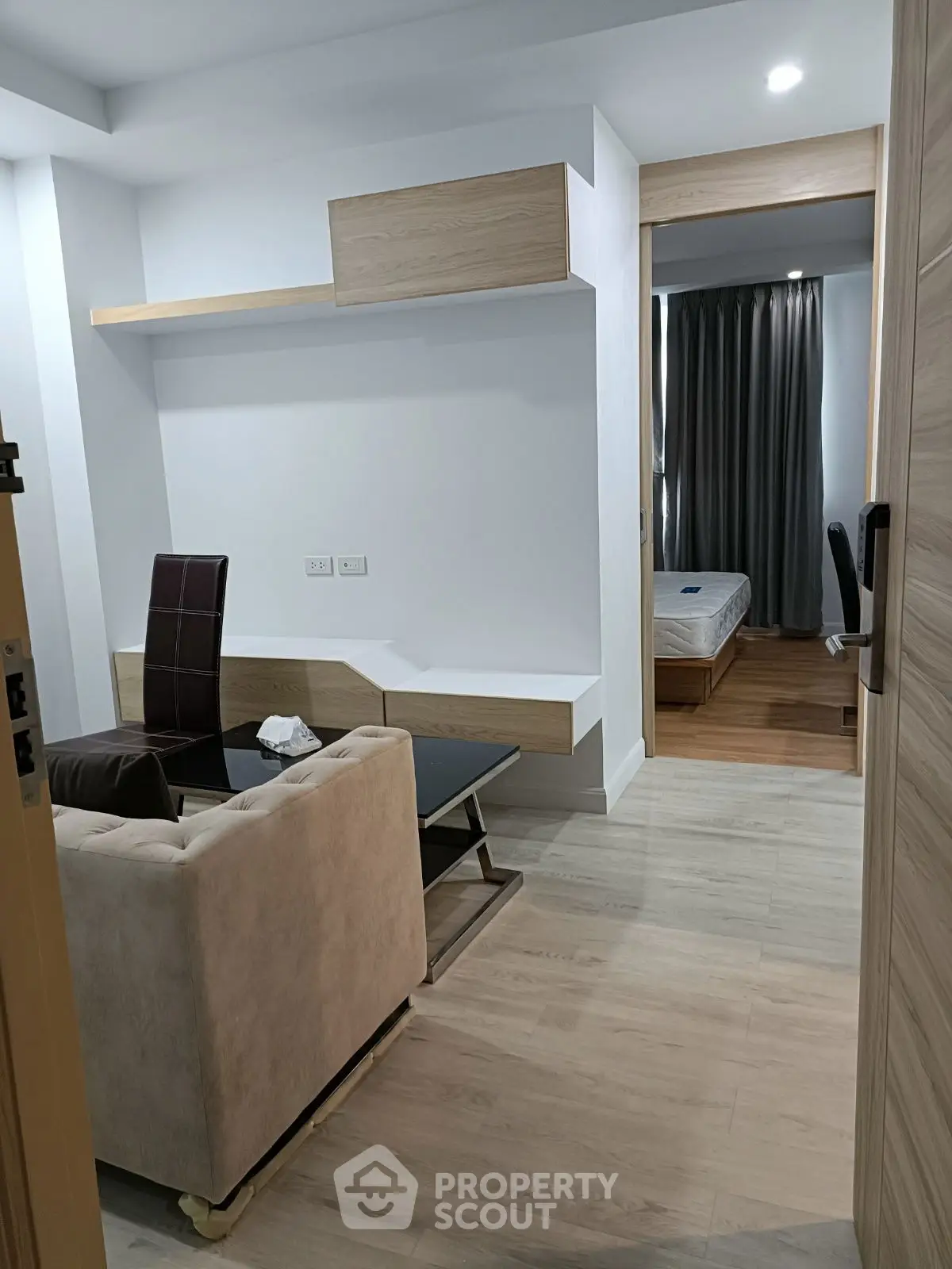 Modern apartment interior with cozy living area and glimpse of bedroom, featuring sleek furniture and wooden flooring.