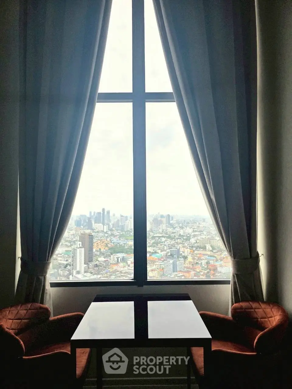 Stunning cityscape view from high-rise apartment window with elegant curtains and cozy seating.