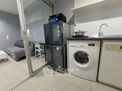 Modern apartment kitchen with fridge and washing machine, open layout to living room.