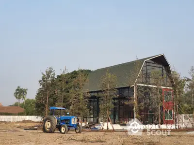 Modern barn-style house under construction with a blue tractor in the foreground