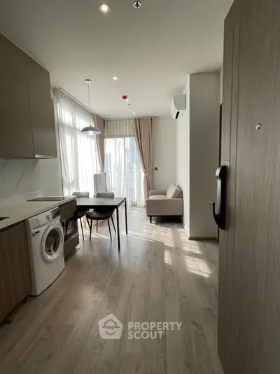 Modern apartment interior with washing machine and dining area, featuring large windows and natural light.