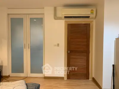Cozy and well-lit living space featuring modern air conditioning, elegant wooden door, and sliding glass doors leading to a balcony, perfect for urban living.