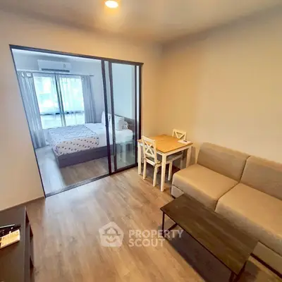 Modern apartment with cozy living room and bedroom separated by glass doors, featuring stylish furniture.