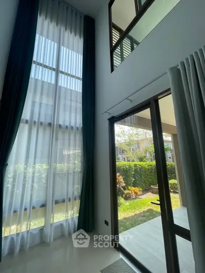 Spacious living room with high ceilings and garden view, featuring elegant floor-to-ceiling windows.