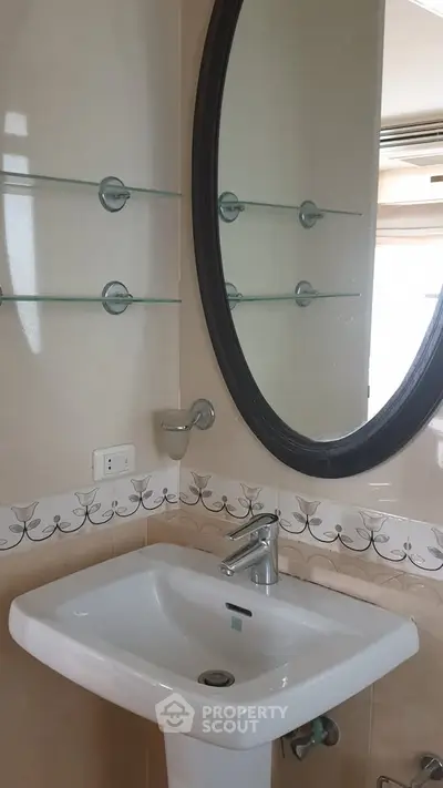Elegant bathroom with modern sink and oval mirror, featuring stylish tile design.