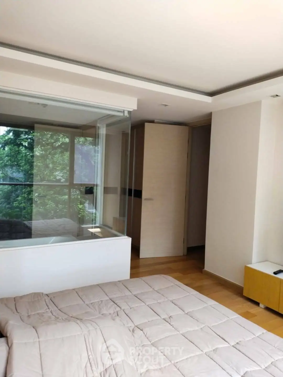 Modern bedroom with large window and natural light, featuring a cozy bed and wooden flooring.