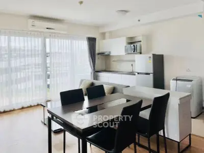 Modern open-plan living room with dining area and kitchen, featuring sleek furniture and large windows.