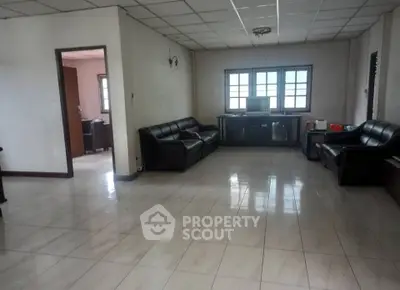 Spacious living room with tiled flooring and leather sofas, featuring large windows for natural light.