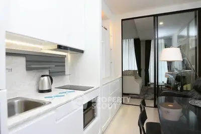 Modern kitchen with sleek white cabinets and cozy living area in open layout apartment.