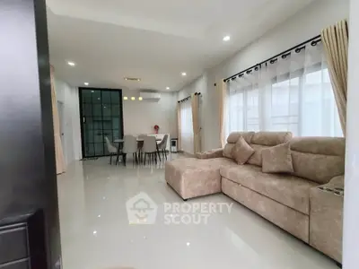 Spacious modern living room with plush sofa and dining area, featuring large windows and elegant decor.