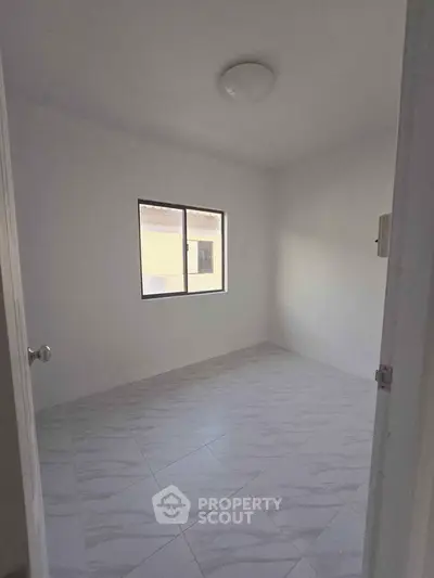 Spacious empty room with tiled floor and window, perfect for customization.