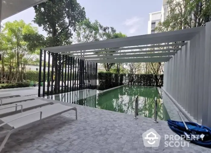 Inviting modern pool area with elegant loungers, shaded pergola, and lush greenery, perfect for relaxation and entertainment.