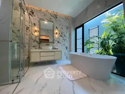 Luxurious marble bathroom with freestanding bathtub and large window view of greenery.