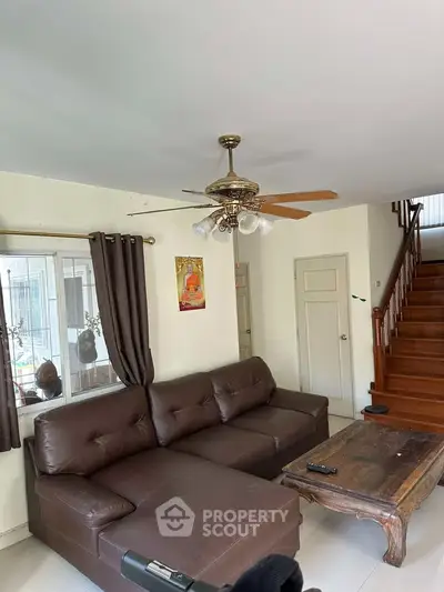 Spacious living room with brown leather sofa and wooden staircase