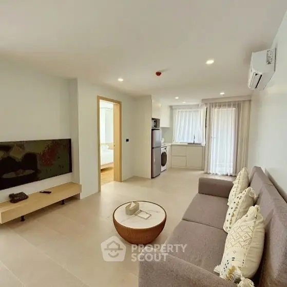 Modern living room with open layout, featuring a cozy sofa, wall-mounted TV, and adjacent kitchen area.