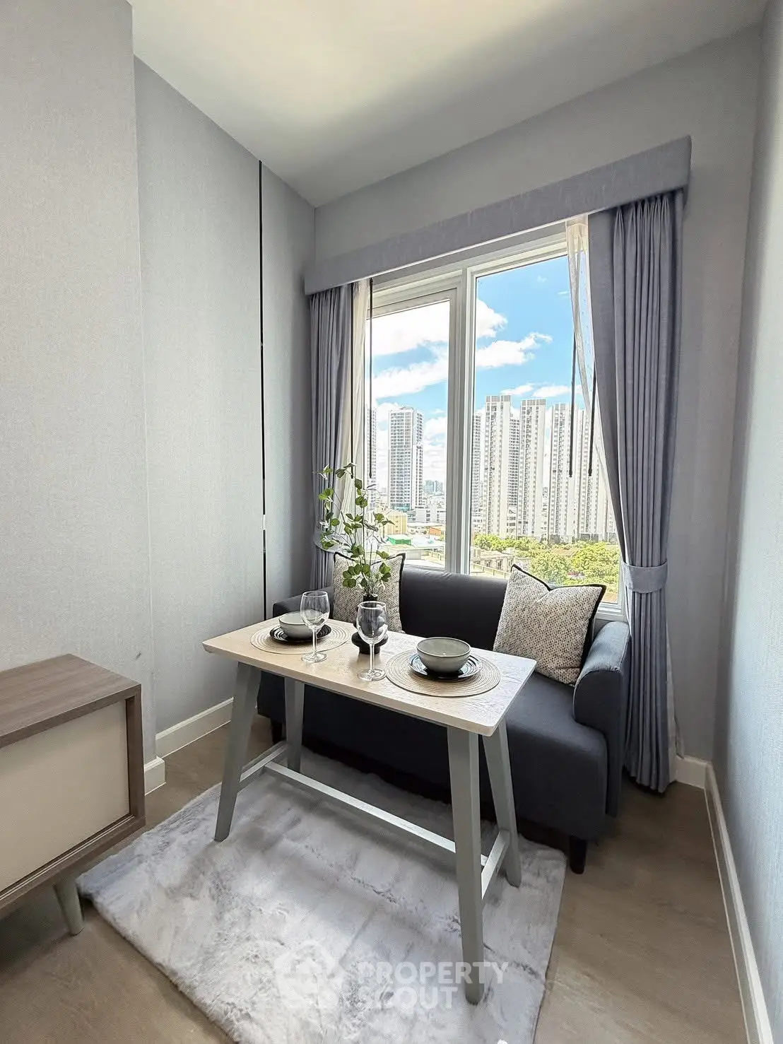 Cozy living room with city view, featuring a stylish sofa and dining setup by the window.