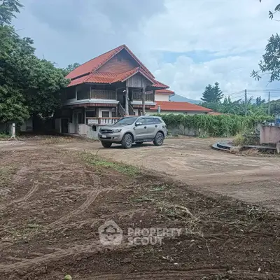 Charming countryside house with red roof and spacious driveway, perfect for serene living.