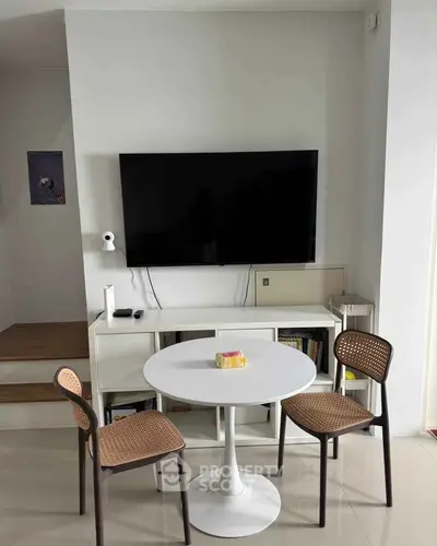 Modern living room with wall-mounted TV, sleek white table, and stylish chairs, perfect for cozy gatherings.