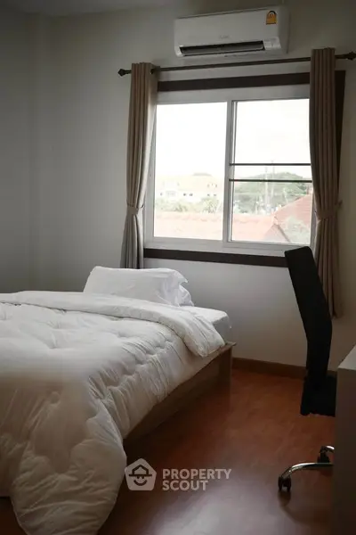 Cozy bedroom with wooden flooring and large window offering natural light.