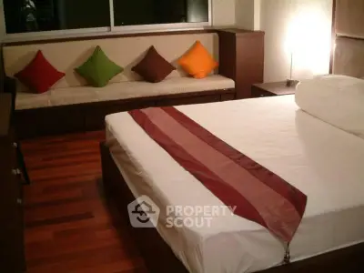 Cozy bedroom with wooden flooring and colorful cushions, perfect for relaxation.