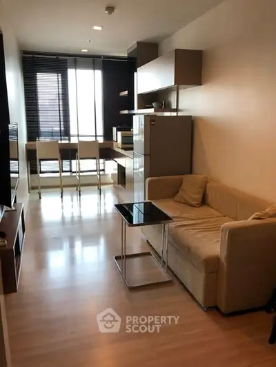 Modern open-layout living room with kitchen, featuring sleek furniture and natural light.