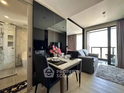 Modern open-plan living room with dining area and glass-walled bathroom, featuring sleek decor and natural light.