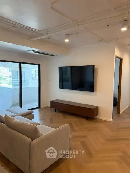 Modern living room with sleek design and large TV, featuring a cozy sofa and access to a balcony.
