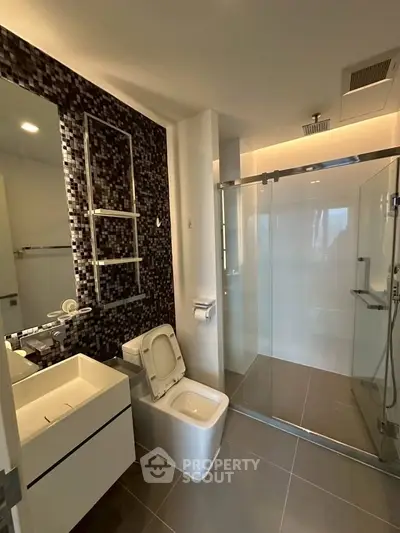 Modern bathroom with sleek design, glass shower, and stylish mosaic wall tiles.