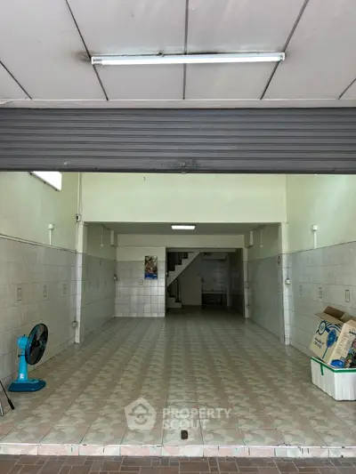 Spacious tiled garage with open shutter and staircase, ideal for storage or workshop.