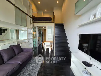 Modern loft apartment with sleek black staircase and cozy living area, featuring a mezzanine bedroom and stylish decor.
