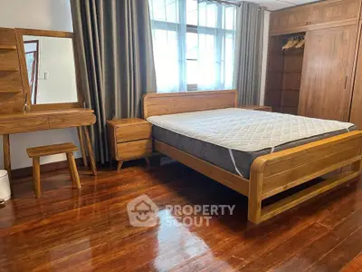 Spacious bedroom with wooden furniture and large window for natural light.