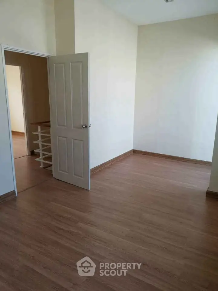 Spacious empty room with wooden flooring and open door leading to another room.