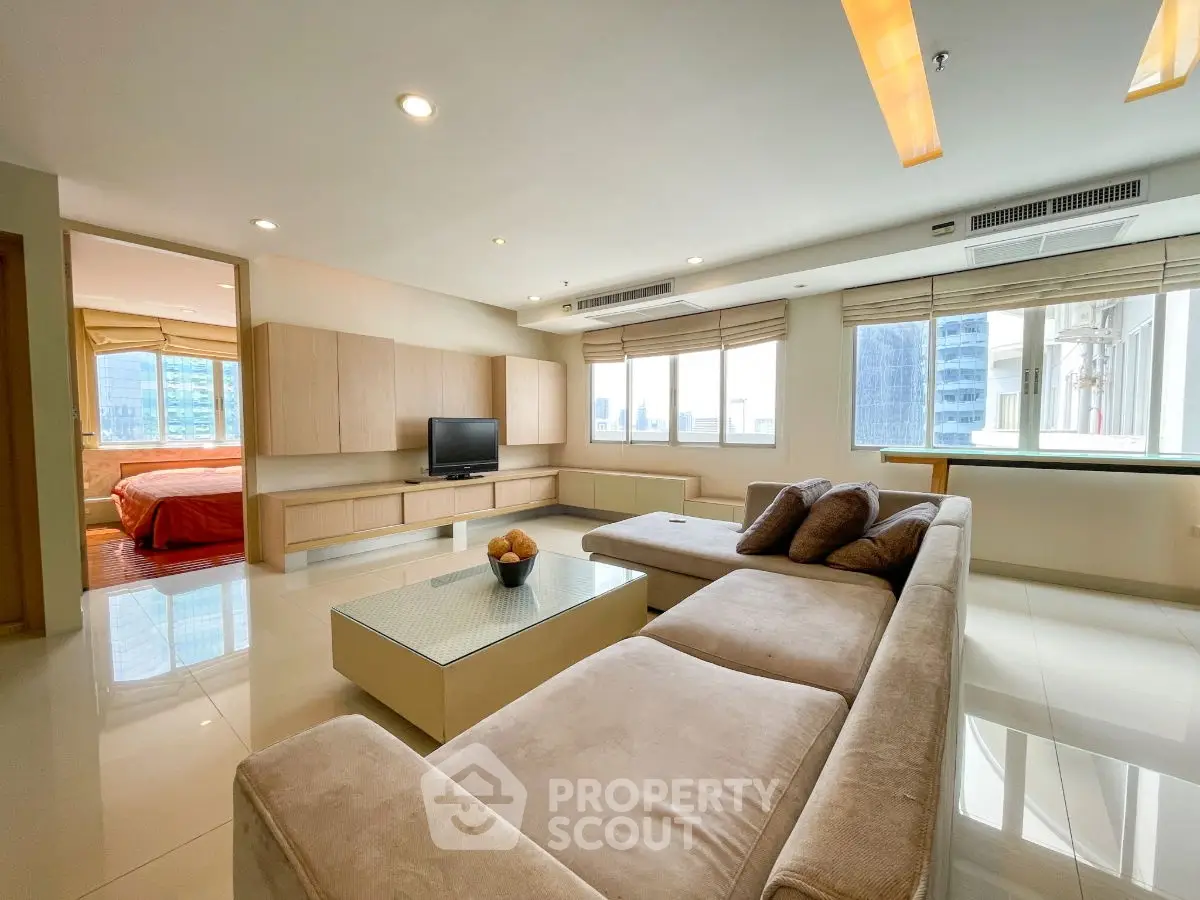 Spacious modern living room with large windows and city view, featuring a cozy sectional sofa and sleek entertainment unit.