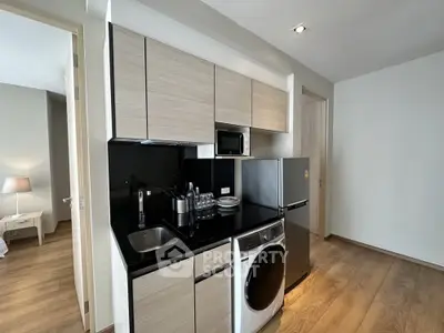 Modern compact kitchen with sleek appliances and wooden flooring in a cozy apartment.