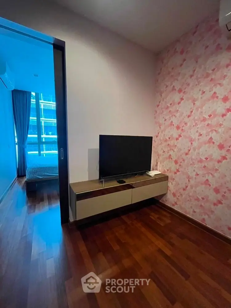Modern living space with stylish TV unit and floral accent wall, featuring wooden flooring and a glimpse of a bedroom.