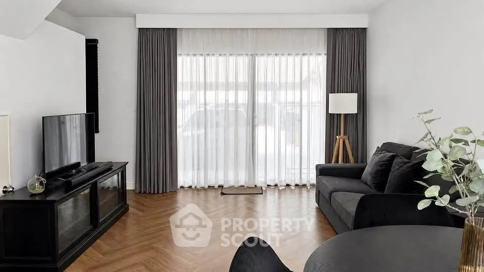 Elegant living room with modern decor and large window, featuring stylish furniture and natural light.