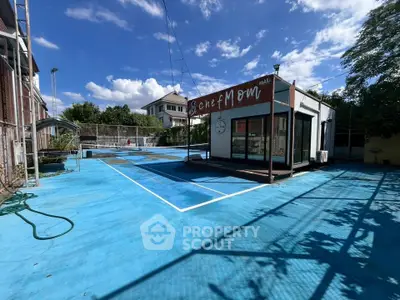 Spacious outdoor area with blue flooring and a small building, ideal for commercial use.