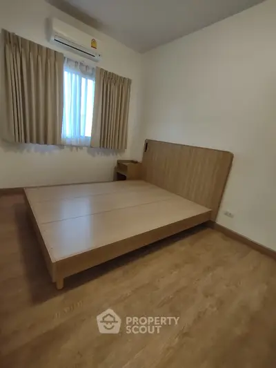 Minimalist bedroom with wooden flooring and bed frame, featuring air conditioning and natural light.