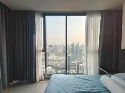 Luxurious bedroom with stunning city view through large windows, featuring elegant curtains and cozy bedding.