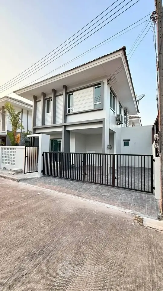 Modern two-story house with sleek design and gated driveway in a suburban neighborhood.