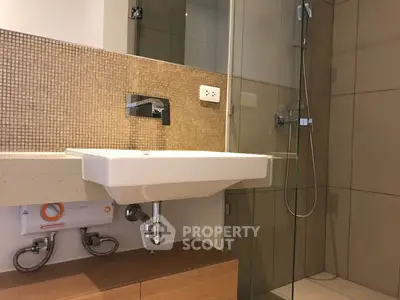 Modern bathroom with sleek sink and glass shower enclosure in contemporary apartment.