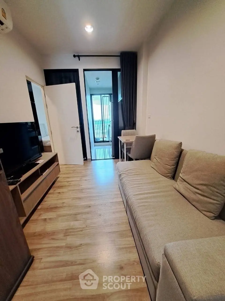 Modern living room with cozy sofa and wooden flooring, leading to a balcony with natural light.