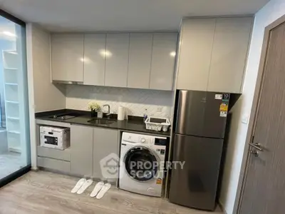 Modern kitchen with sleek cabinets, washing machine, and stainless steel fridge in compact layout.